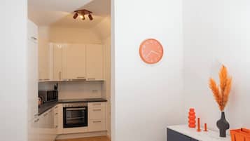 A modern kitchen with white cabinets, a microwave, and a black oven. There's a wooden herringbone floor and a grey carpet.