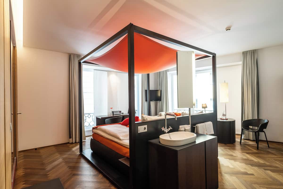 Un hotel moderno con una cama con dosel, una mesita de noche con lámpara, un espejo grande y vistas a la ciudad.