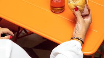 Una persona sosteniendo un sándwich y una jarra de cerveza sobre una mesa anaranjada.
