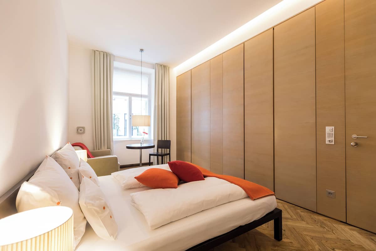 Habitación de hotel moderna con cama, mesita de noche, lámpara y vistas al exterior.