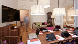 Una habitación de hotel moderna con un escritorio de madera, una computadora portátil, una tableta, un televisor y un sofá.