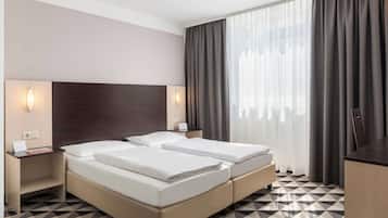 A hotel room with a double bed, bedside tables, a desk, and a large window with curtains.