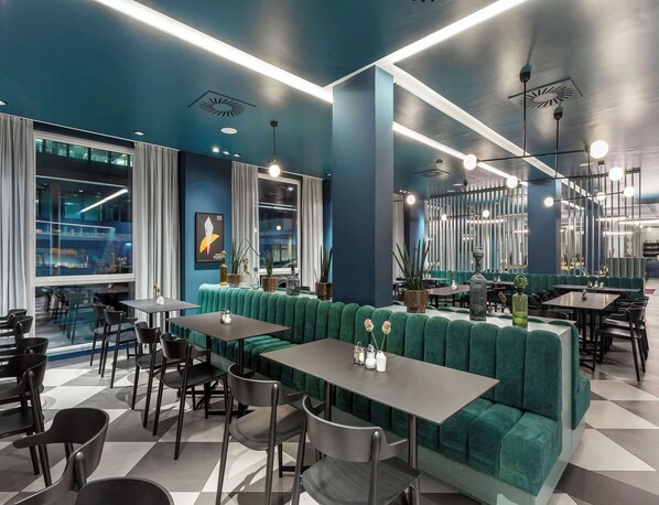 Un interior de restaurante moderno con cabinas tapizadas de verde, sillas negras y piso de cuadros.