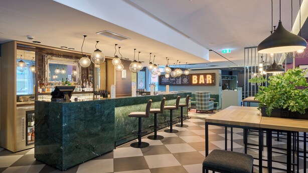 A bar area with a marble counter, bar stools, hanging lights, and a sign that reads 'BAR'.