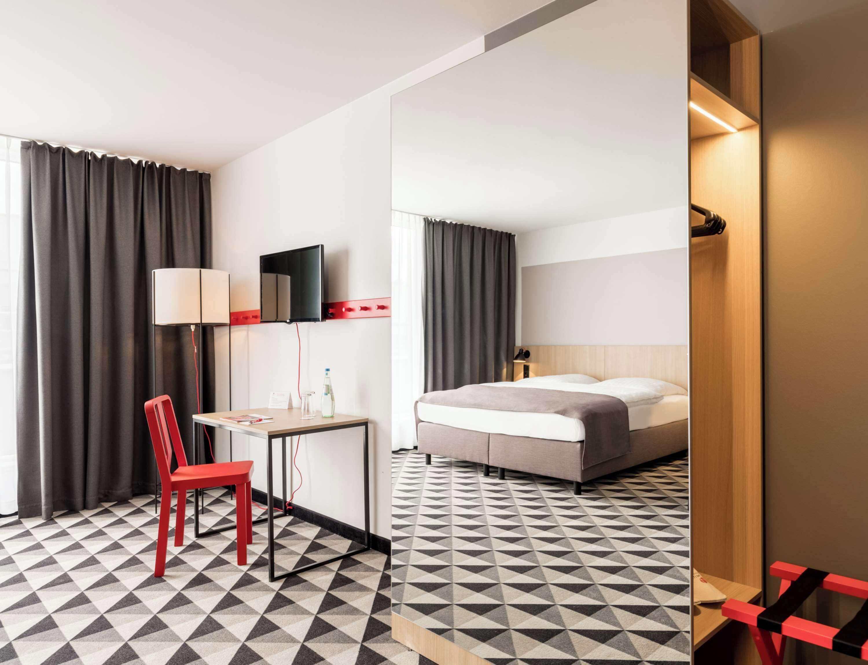 Ein Hotelzimmer mit Bett, Schreibtisch, Stuhl, Fernseher und Spiegel.