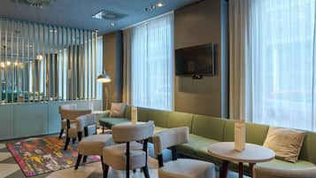 A modern hotel lobby with seating, a TV, and a patterned rug.