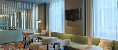 A modern hotel lobby with seating, a TV, and a patterned rug.