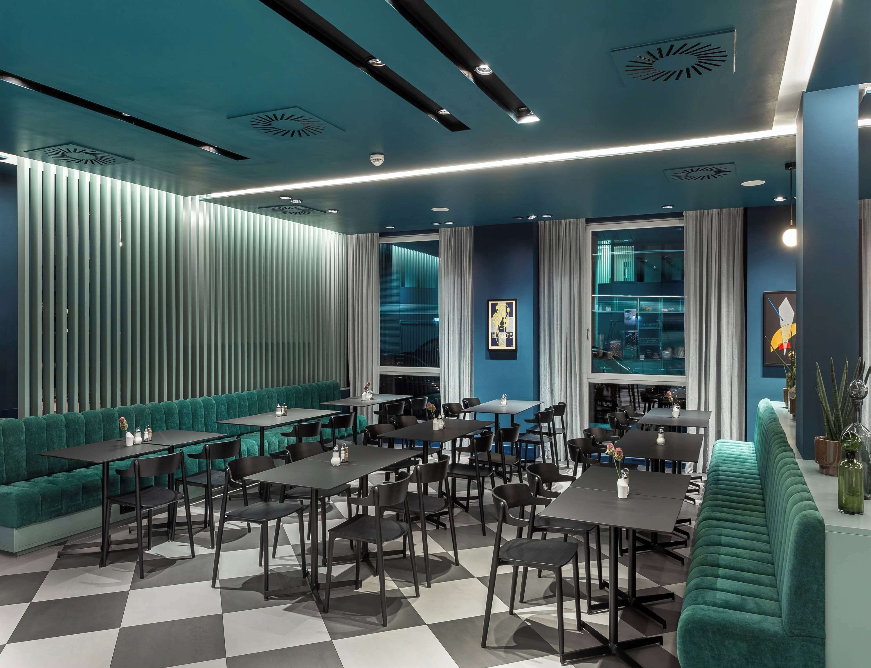 A modern restaurant with a checkered floor, teal upholstered seating, and a variety of table and chair arrangements.