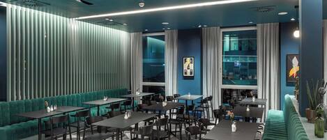 A modern restaurant with a checkered floor, teal upholstered seating, and a variety of table and chair arrangements.