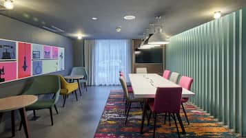 Una sala de reuniones moderna con una larga mesa, sillas de colores, una alfombra estampada y una pared con varios iconos.