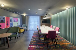 Una sala de reuniones moderna con una larga mesa, sillas de colores, una alfombra estampada y una pared con varios iconos.