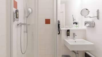 Ein modernes Badezimmer mit einer gläsernen Duschkabine, einem weißen Waschbecken mit Spiegel und einem Handtuchspender.