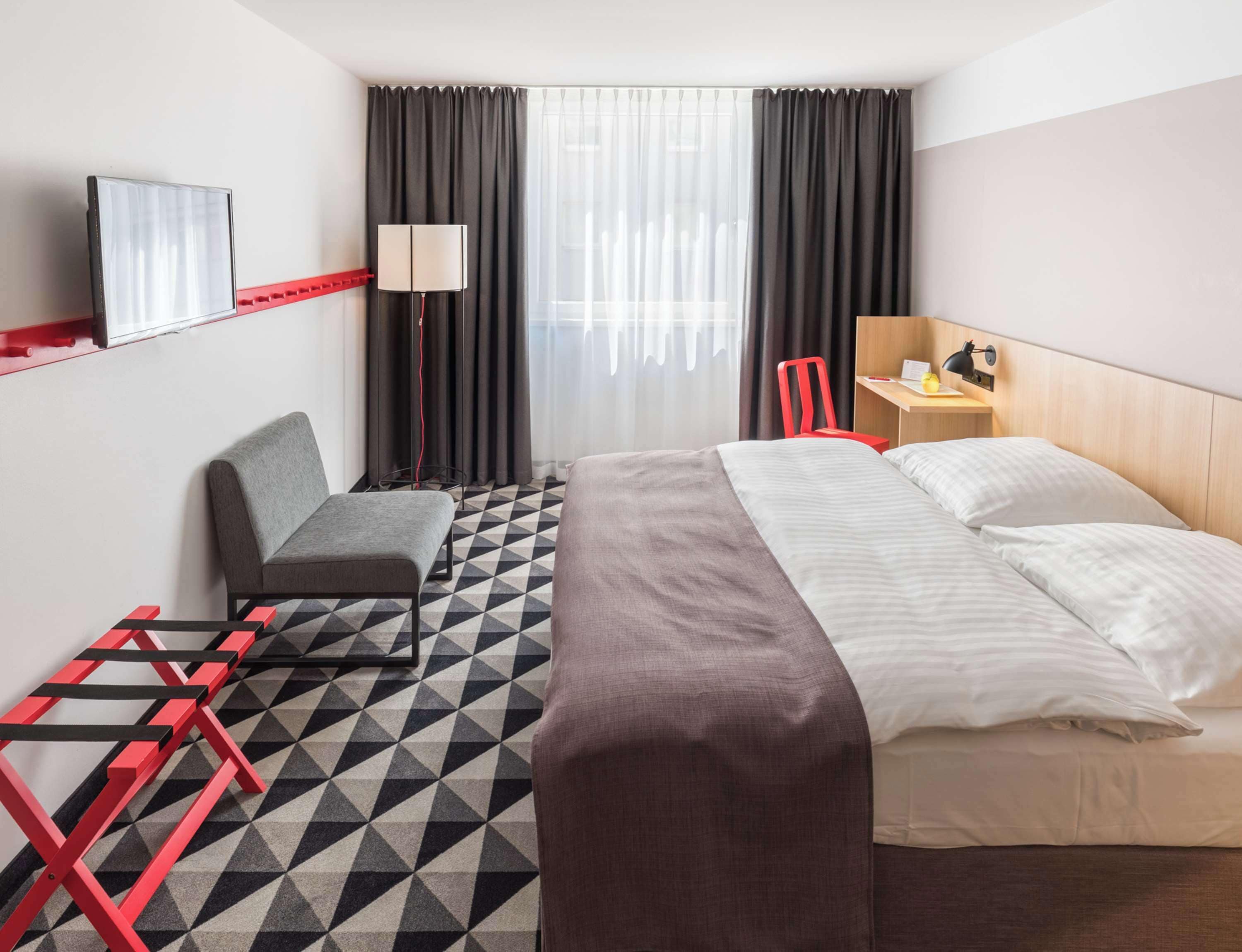 Habitación de hotel con cama, escritorio, silla, lámpara y vista al exterior a través de la ventana.