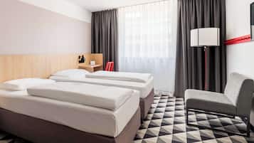 A hotel room with two beds, a desk, a chair, a lamp, and a large window with curtains.