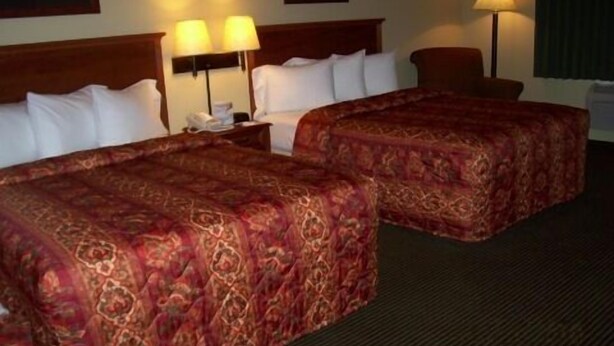 A hotel room with two beds, a nightstand with a lamp, and a chair.