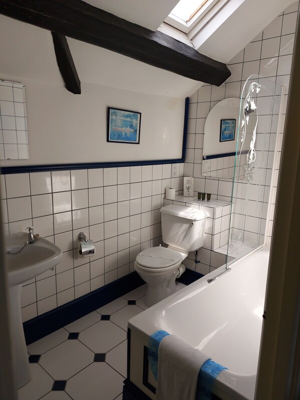 A bathroom with a white sink, toilet, and bathtub. There are two framed pictures on the wall, and the floor has a black and white tile pattern.
