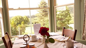 Una mesa dispuesta para el desayuno, un menú, un florero con una rosa roja y una vista panorámica a través de amplios ventanales.