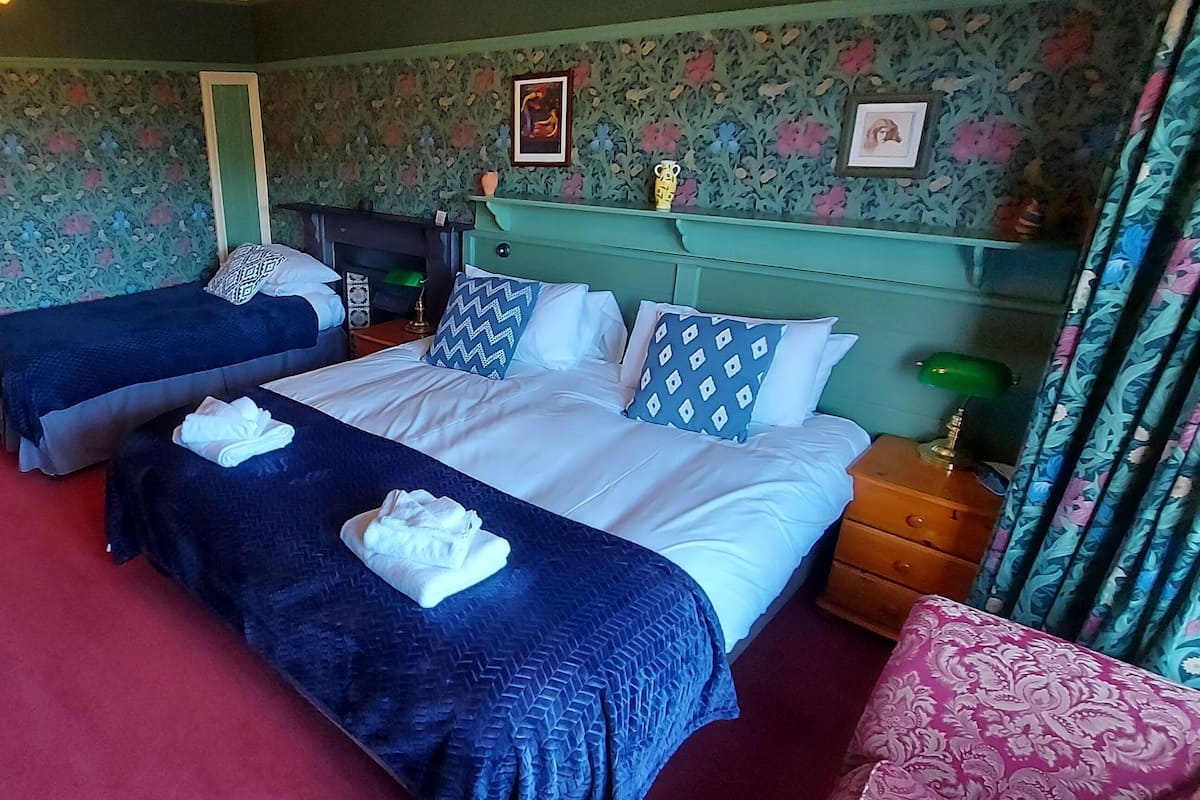 Ein Hotelzimmer mit zwei Betten, einem roten Teppich, blumigem Wandpapier und einem grünen Kopfteil.