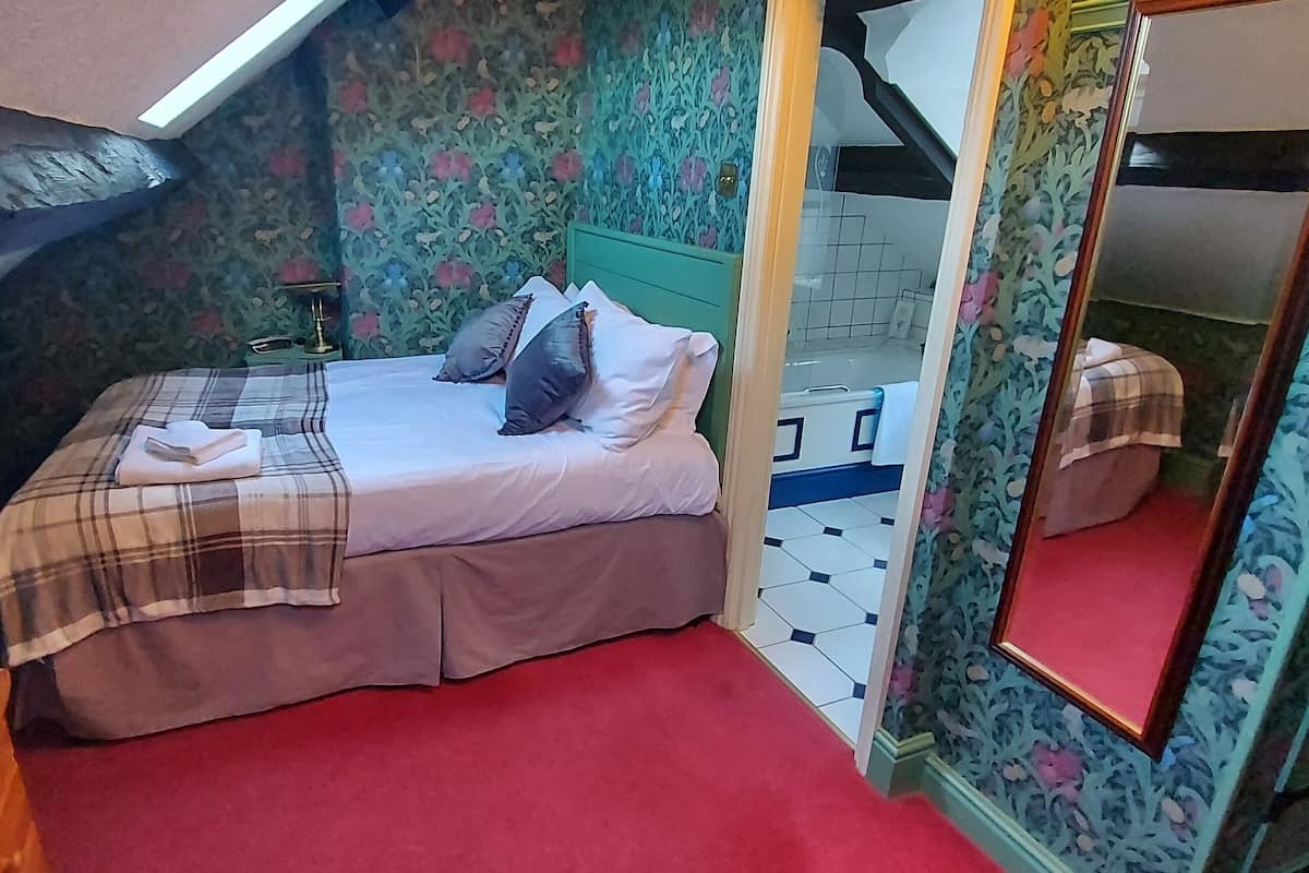 Ein kleines, gemütliches Schlafzimmer mit einem Einzelbett, einem Nachttisch, einem Spiegel und einem Fenster mit Blick ins Freie.