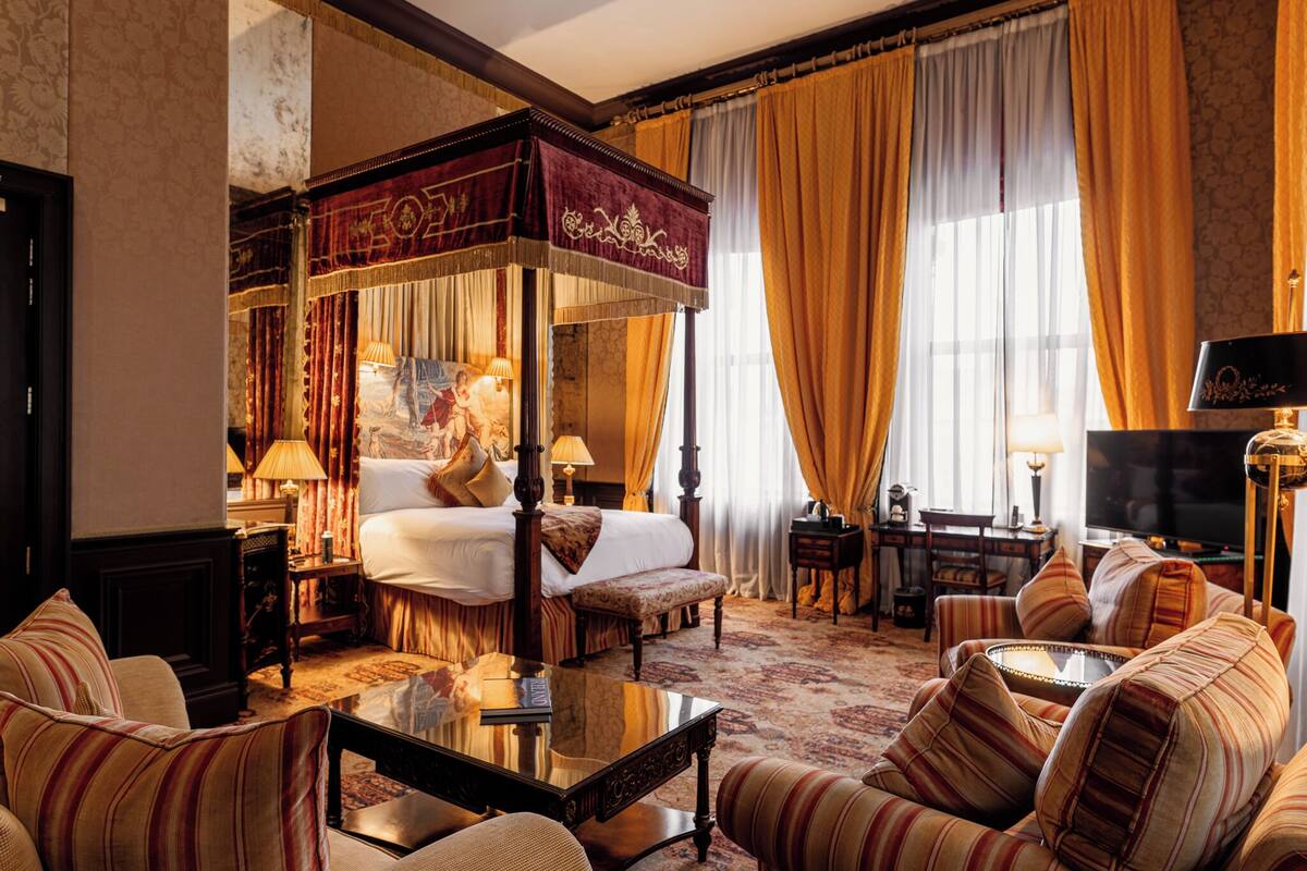A luxurious bedroom with a four-poster bed, a sitting area with striped sofas, and a television.