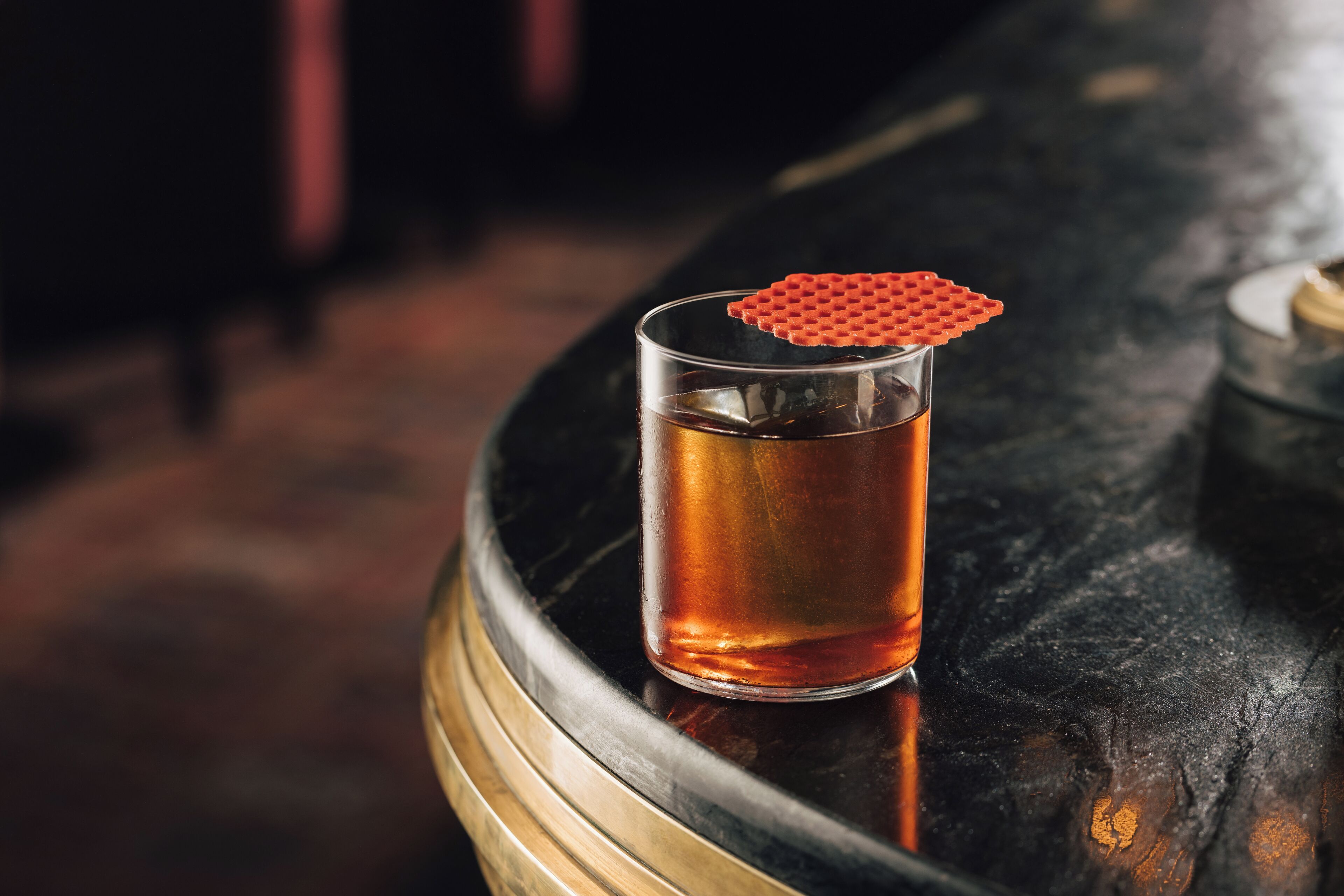 A glass of amber liquid on a dark, round table with a textured red object on top.
