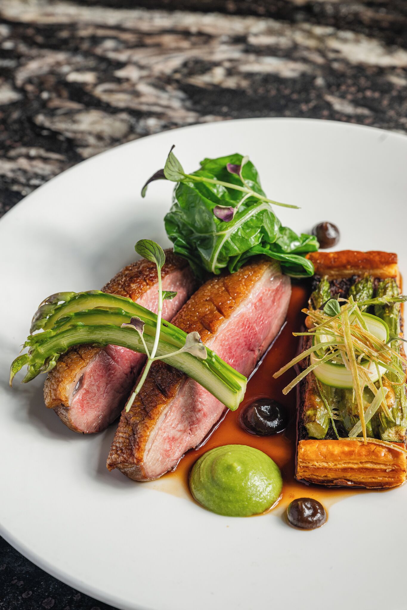 Une assiette de nourriture comprenant du canard, des légumes verts et des sauces.