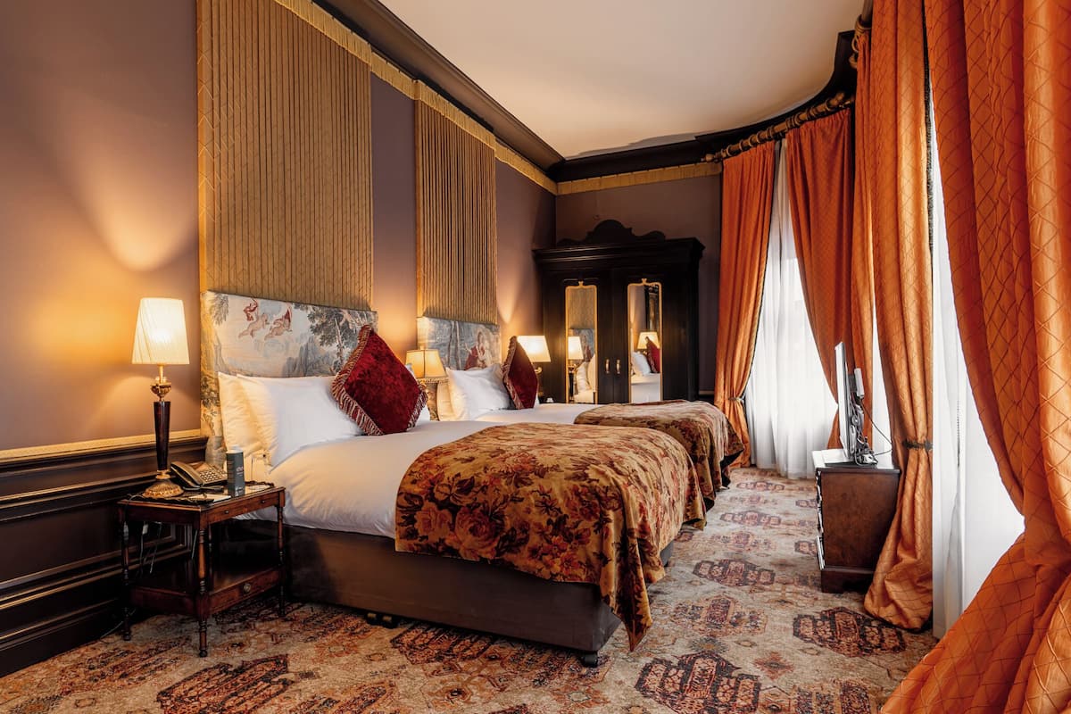 A four-poster bed with floral bedspreads, a nightstand with a lamp, and a large mirror.