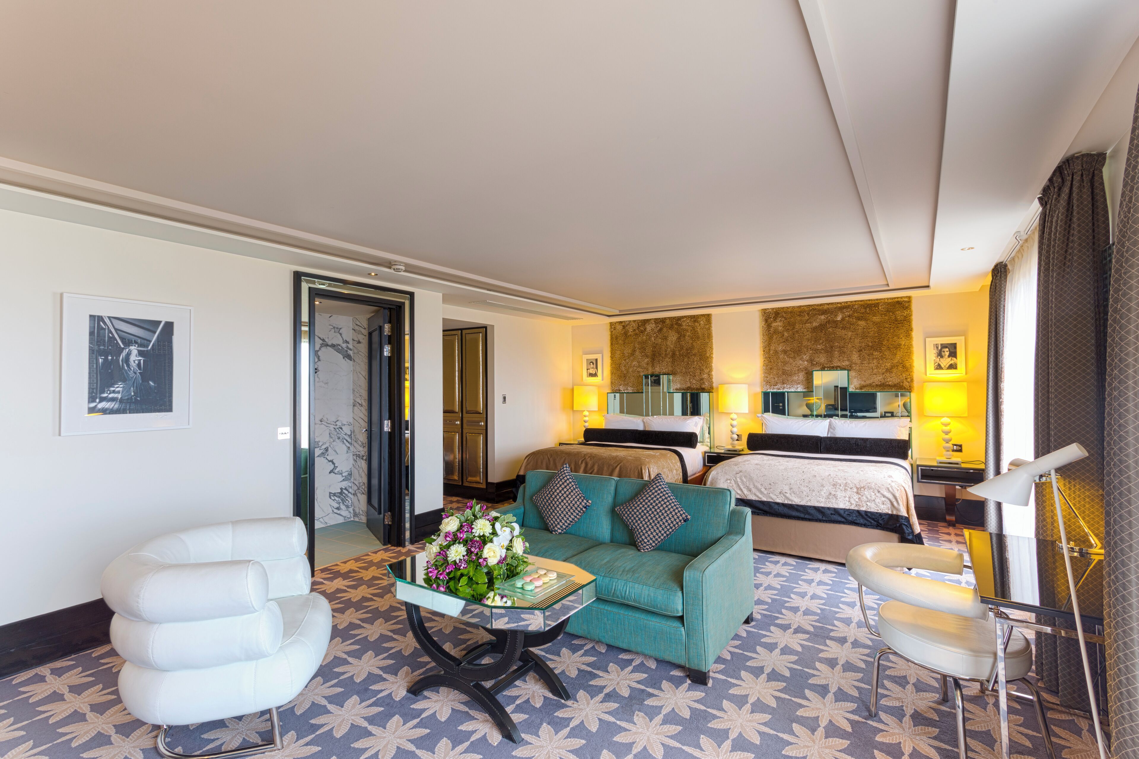 A hotel room with a bed, a sofa, a small table with flowers, and a chair.
