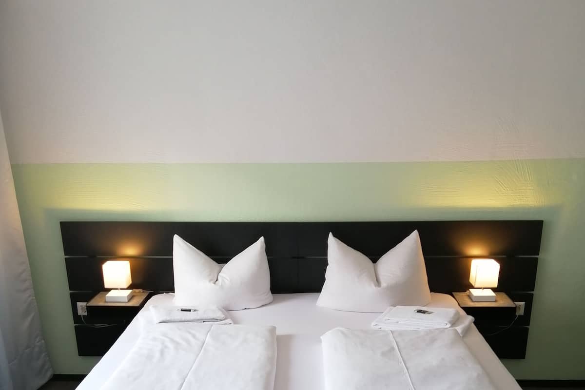 A double bed with two bedside tables, each with a lamp, in a room with a green accent wall.