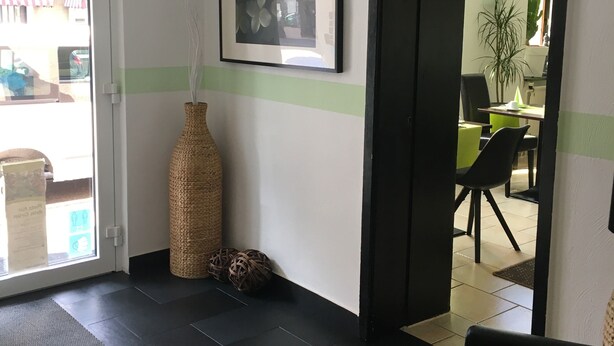 Un espace d’accueil agrémenté d’un grand vase en fibres tressées, d’une œuvre d’art abstraite encadrée et d’une porte donnant sur une salle à manger.