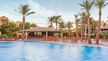 A pool area with palm trees, outdoor seating, and a thatched-roof structure.