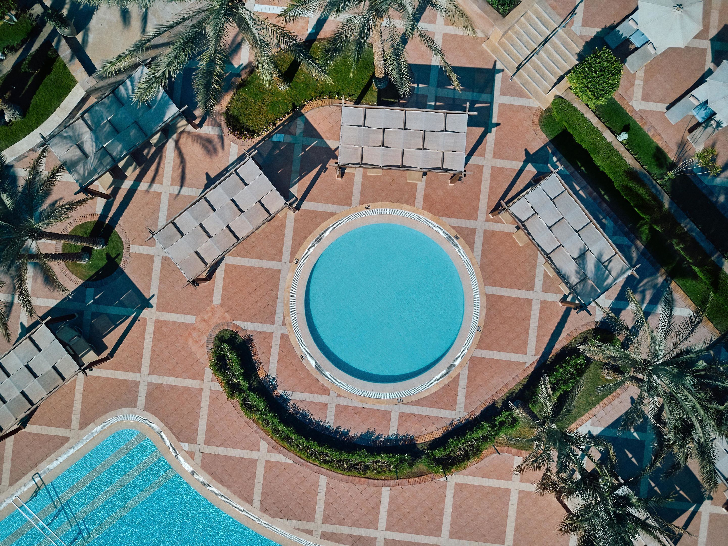 An aerial view of a resort with a central swimming pool, lounge areas, and palm trees.