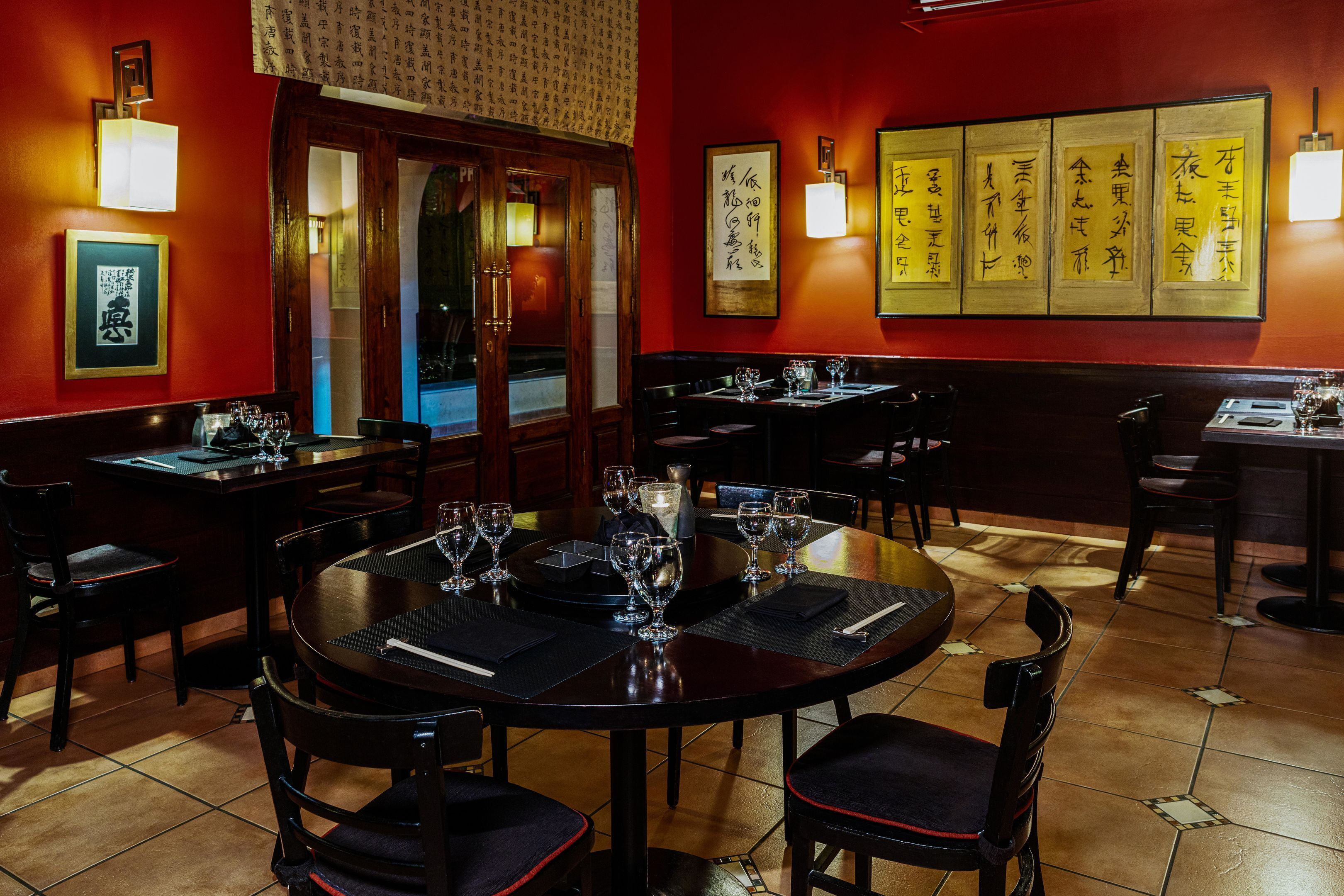 A restaurant interior with wooden tables and chairs, framed calligraphy on the wall, and a tiled floor.