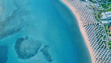 Vista aérea de un resort en la playa, con hileras de sombrillas y sillas, un mar azul y los edificios del resort.