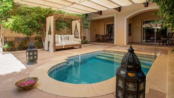 Ein Pool mit Holzterrasse, Sonnensegel und einer Sitzgruppe unter einem Sonnensegel.