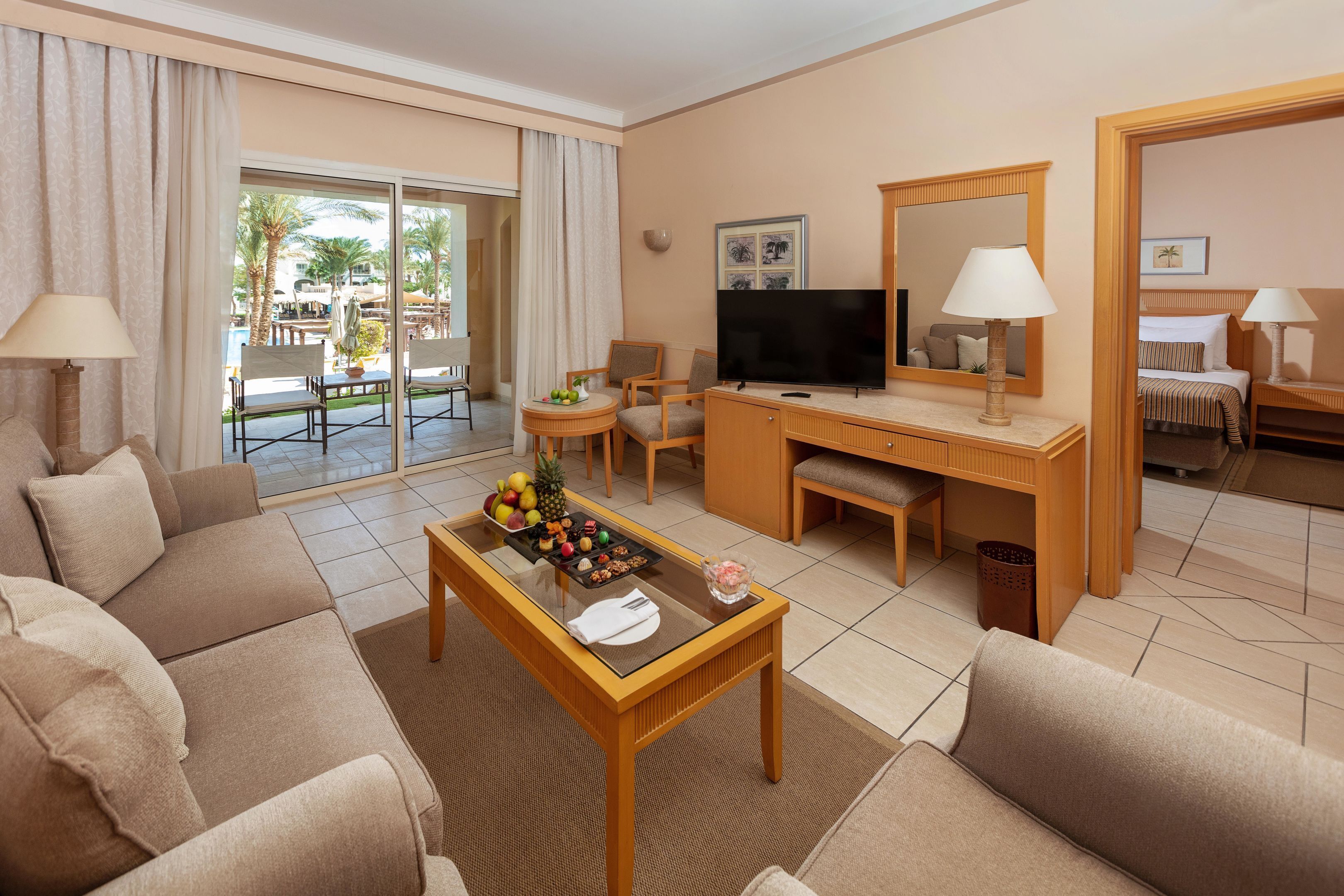 Ein Hotelzimmer mit einer Couch, einem Esstisch mit Obst, einem Fernseher und einem Schreibtisch mit Stuhl.