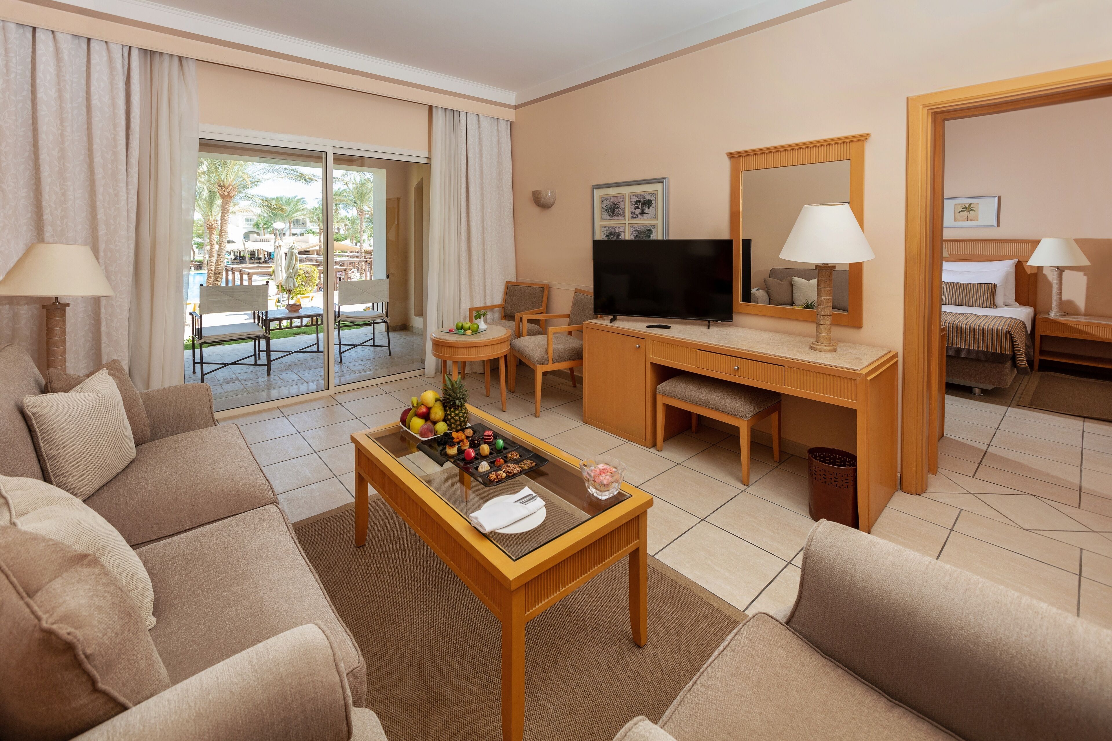 Ein Hotelzimmer mit einer Couch, einem Couchtisch mit Früchten, einem Fernseher und einem Schreibtisch mit einer Lampe.