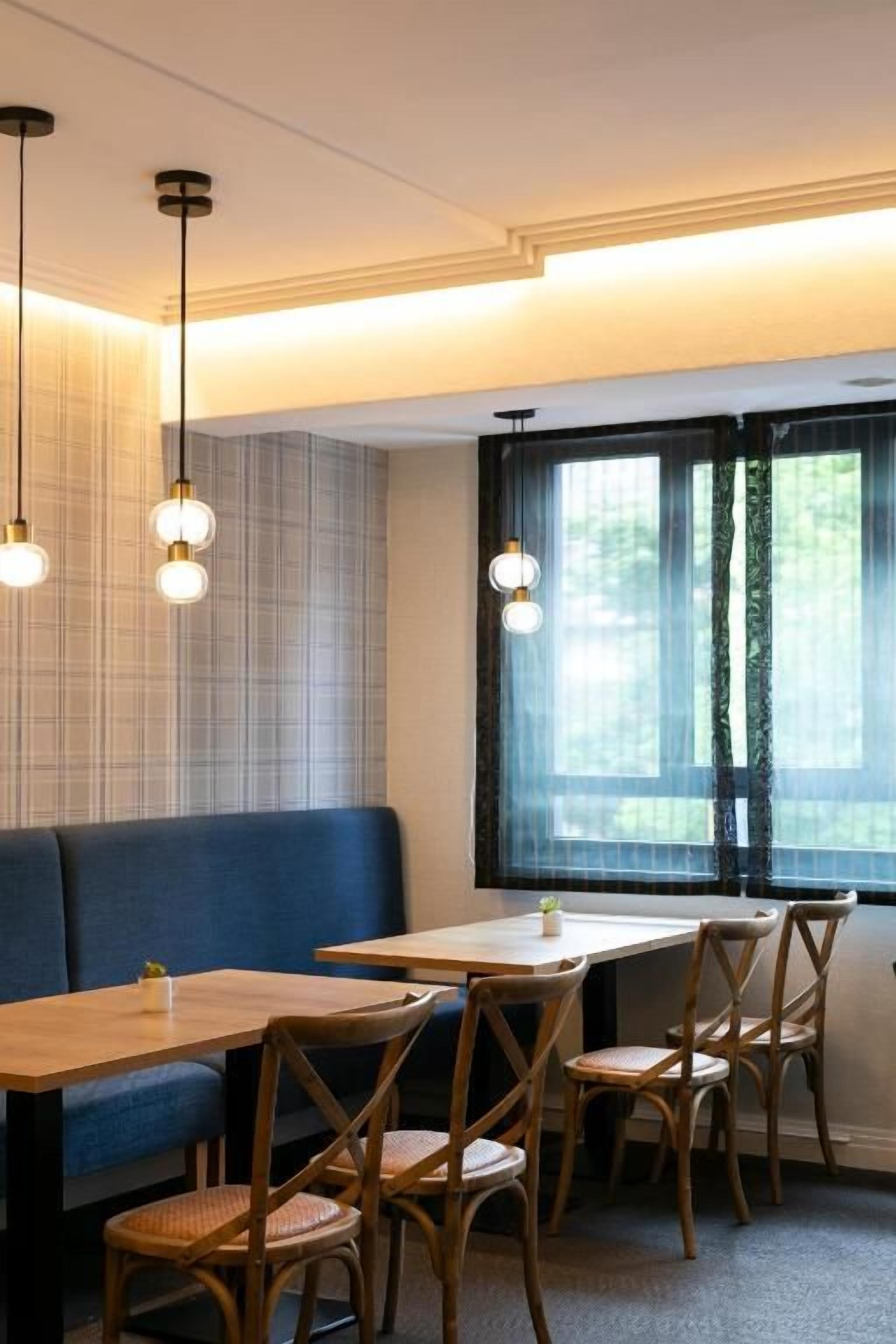 A restaurant interior with a long wooden table, blue cushioned bench, and hanging pendant lights.