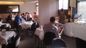 A restaurant with round tables and chairs, a buffet area, and a large window providing natural light. - Hotel Universal (Santiago de Compostela)