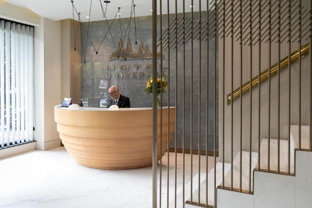 A hotel reception desk with a modern design, a staircase with a railing, and a decorative wall with a logo.