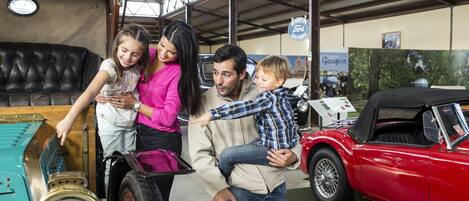 Una familia en un ambiente interior amplio, con un coche antiguo y un gran armario azul.