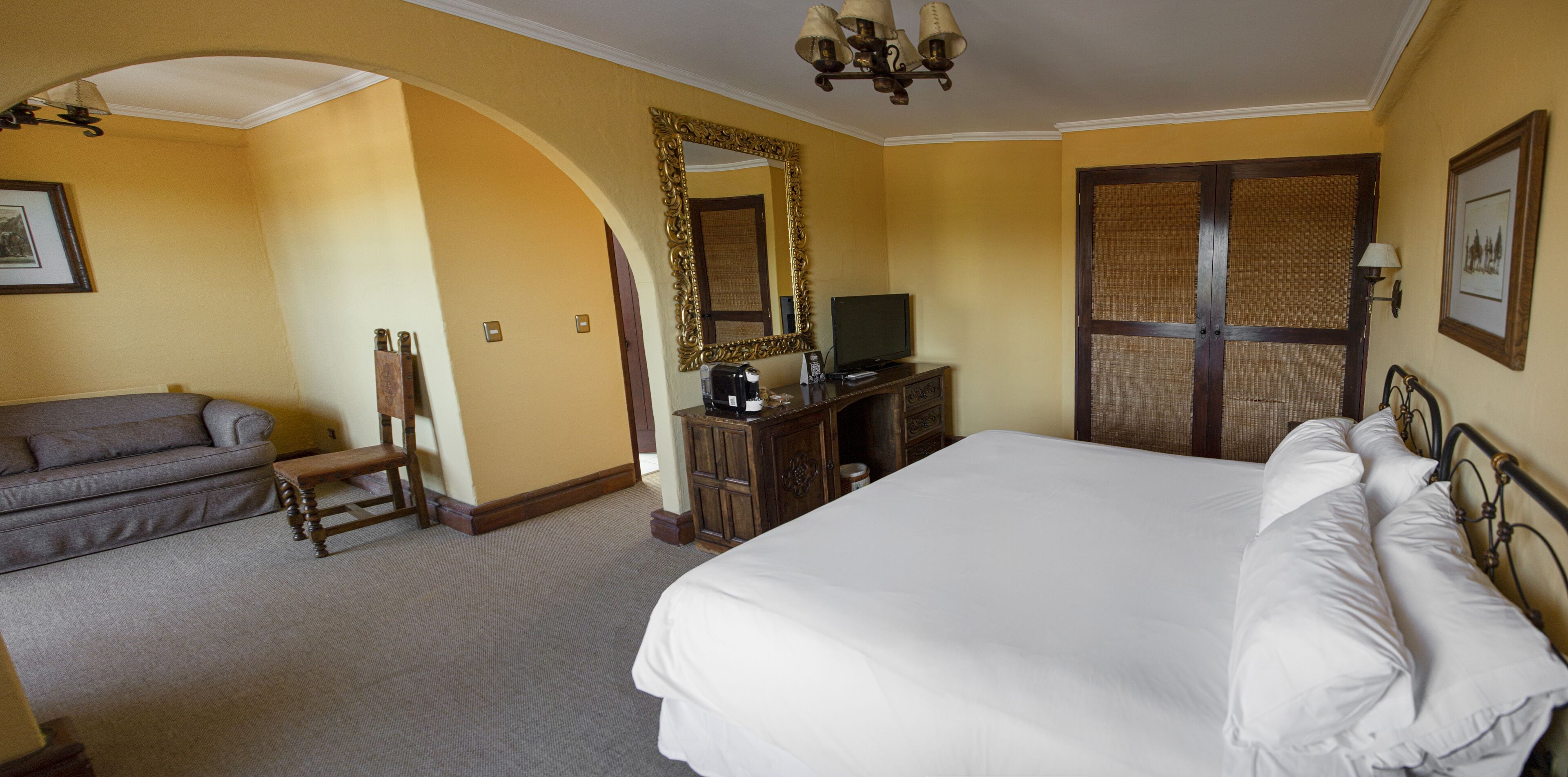 A hotel room with a large bed, a sofa, a dresser, a television, and a mirror.
