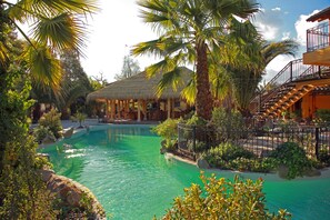 A pool area with a thatched-roof structure, palm trees, and a staircase leading to an upper level. - Santa Cruz Plaza (Santa Cruz)