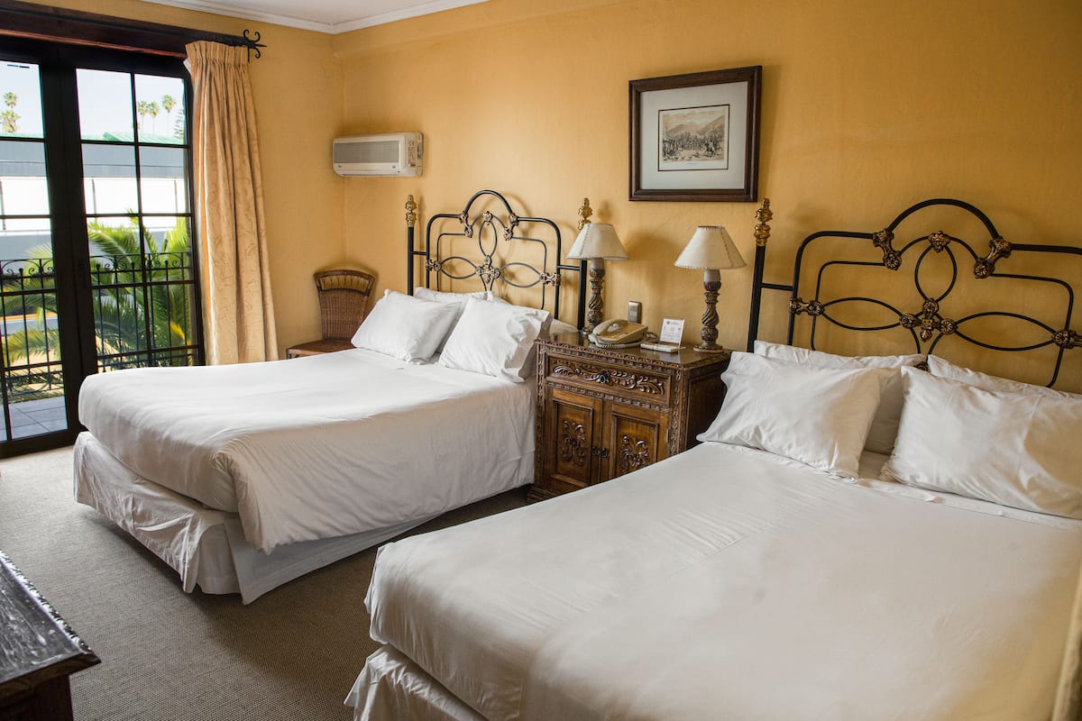 A hotel room with two beds, a wooden nightstand, a lamp, and a framed picture on the wall.