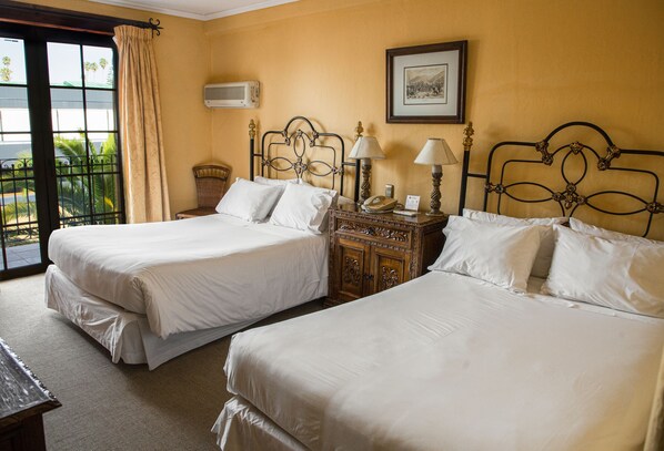 A hotel room with two beds, a wooden nightstand, a lamp, and a framed picture on the wall.