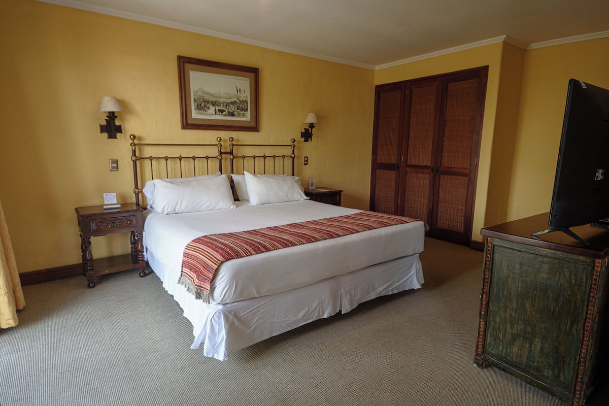 A hotel room with a large bed, two bedside tables, a television, and a wardrobe.