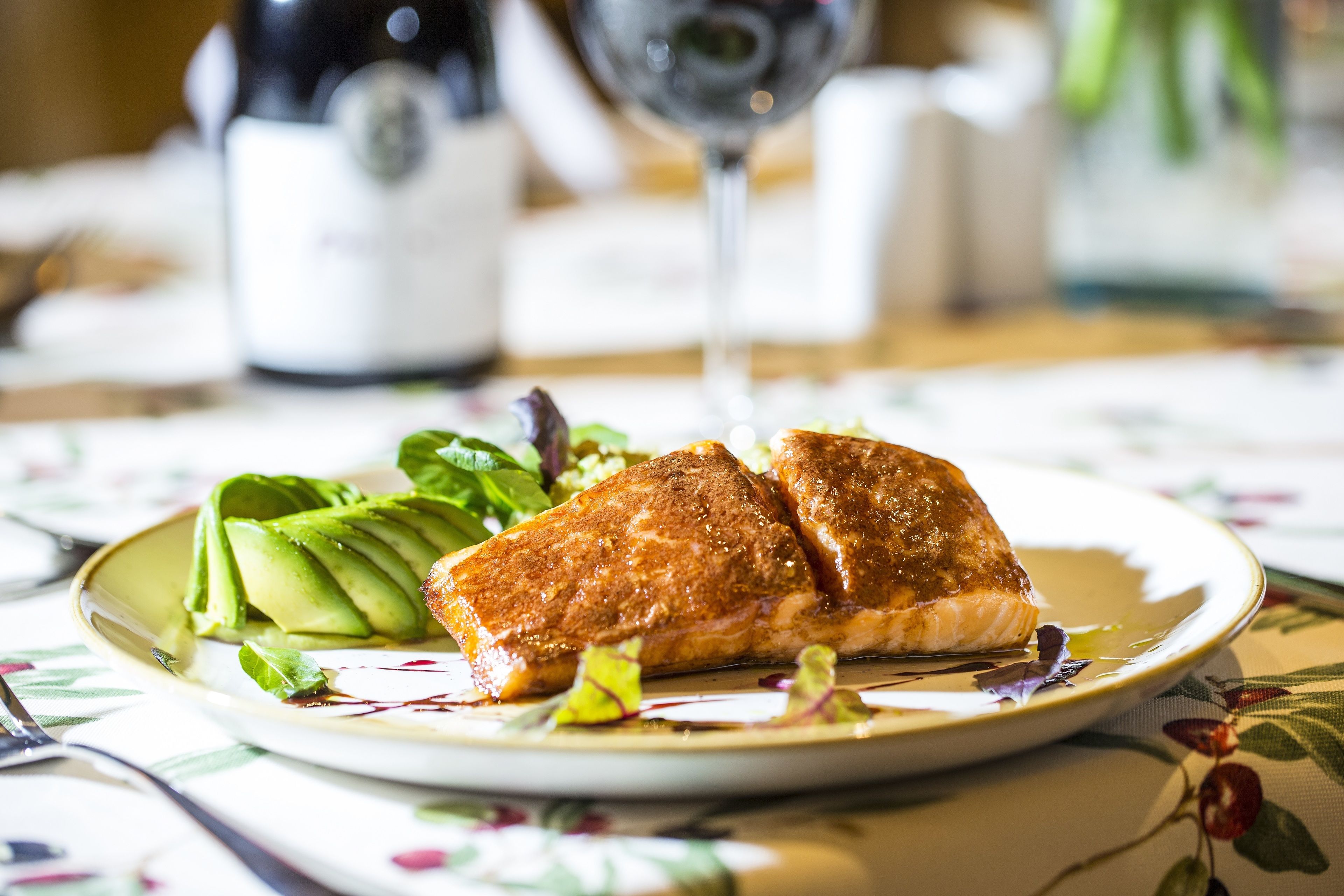Een bord met zalm en avocado op een tafelkleed met bloemen.