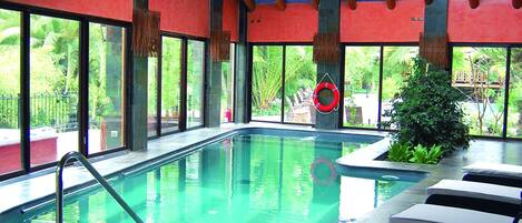 Ein Hallenbad mit klaren Glaswänden, Liegestühlen und einem Rettungsring.