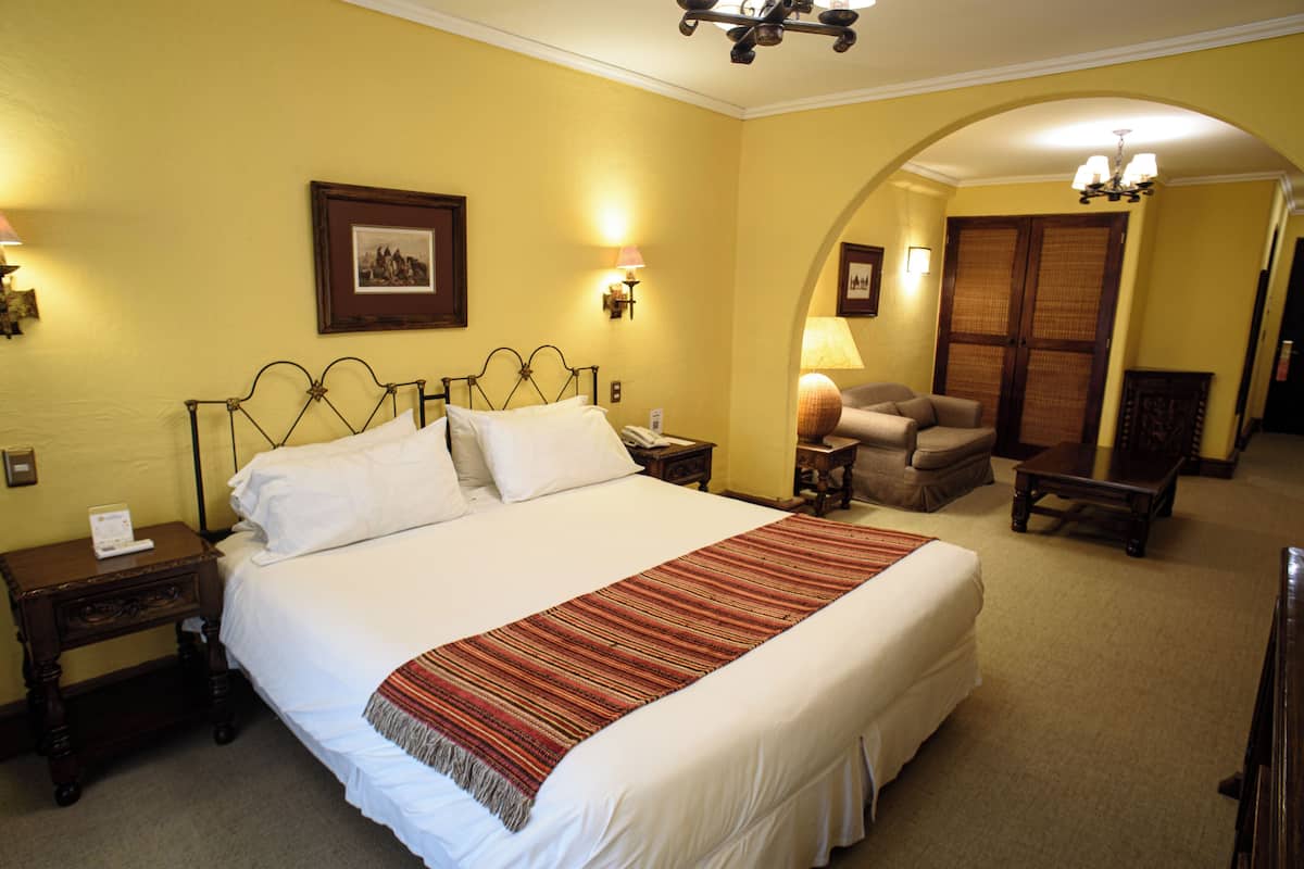 A neatly made bed with a white comforter and a red-striped throw blanket, a wooden nightstand with a lamp, and a framed picture on the wall.