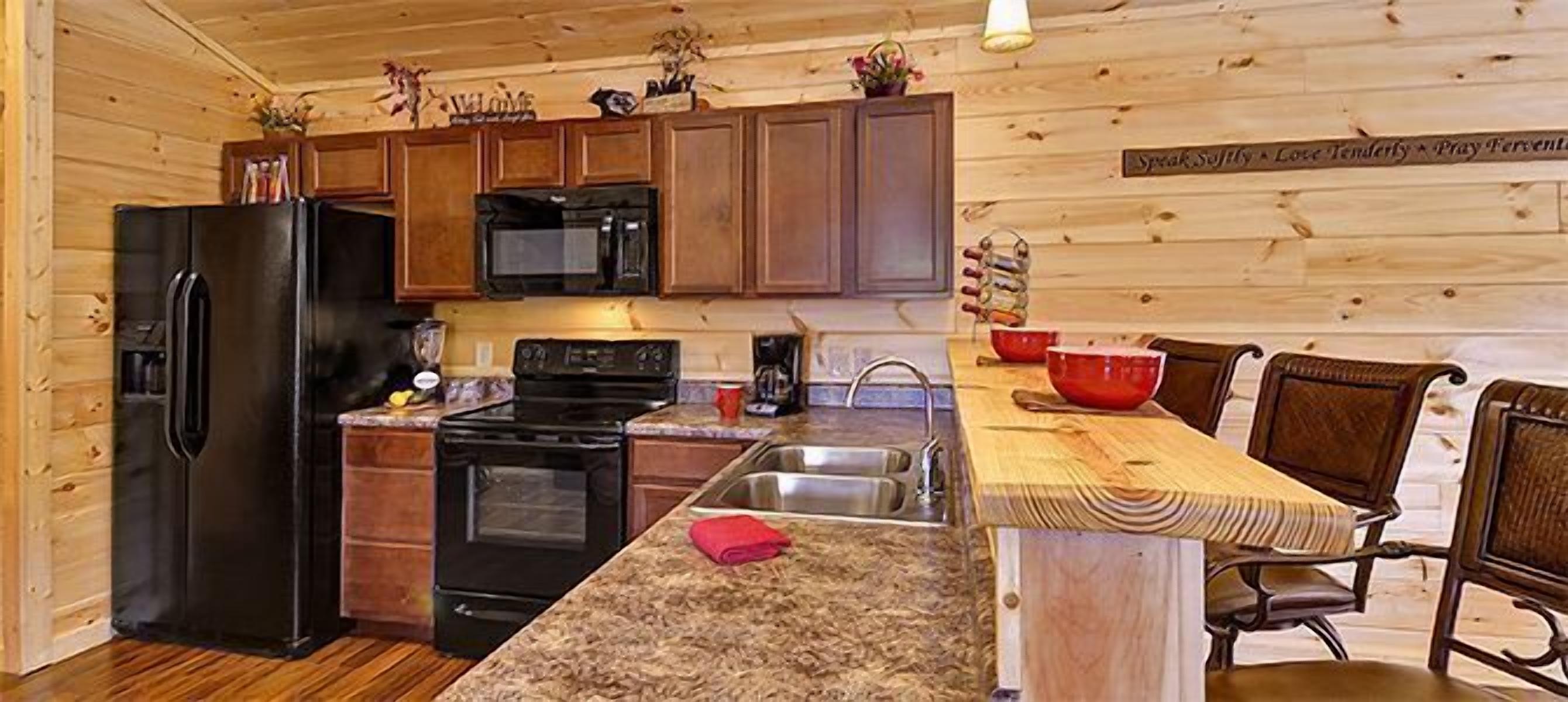 A kitchen with wooden cabinets, a black refrigerator, a microwave, an oven, and a granite countertop.